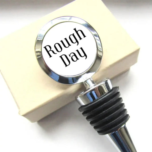 Stopiwr Potel 'Rough Day' mewn golwg agos wrth ymyl blwch anrheg
